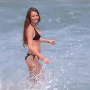 A wrestler takes down a model on a beach.