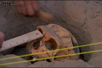 After carefully unearthing a skull fossil someone carelessly breaks it with a pick.